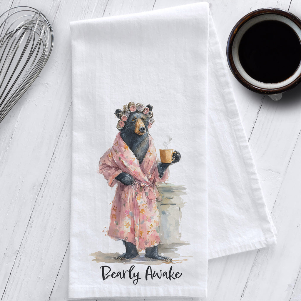 Cotton flour sack tea towel with watercolor art of a grumpy mama bear in a robe and curlers holding coffee, captioned “Bearly Awake.”