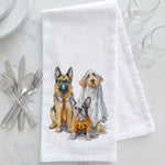 Load image into Gallery viewer, A white kitchen towel with a watercolor illustration of three dogs dressed in Halloween attire, styled on a white marble surface with silver cutlery and glassware.
