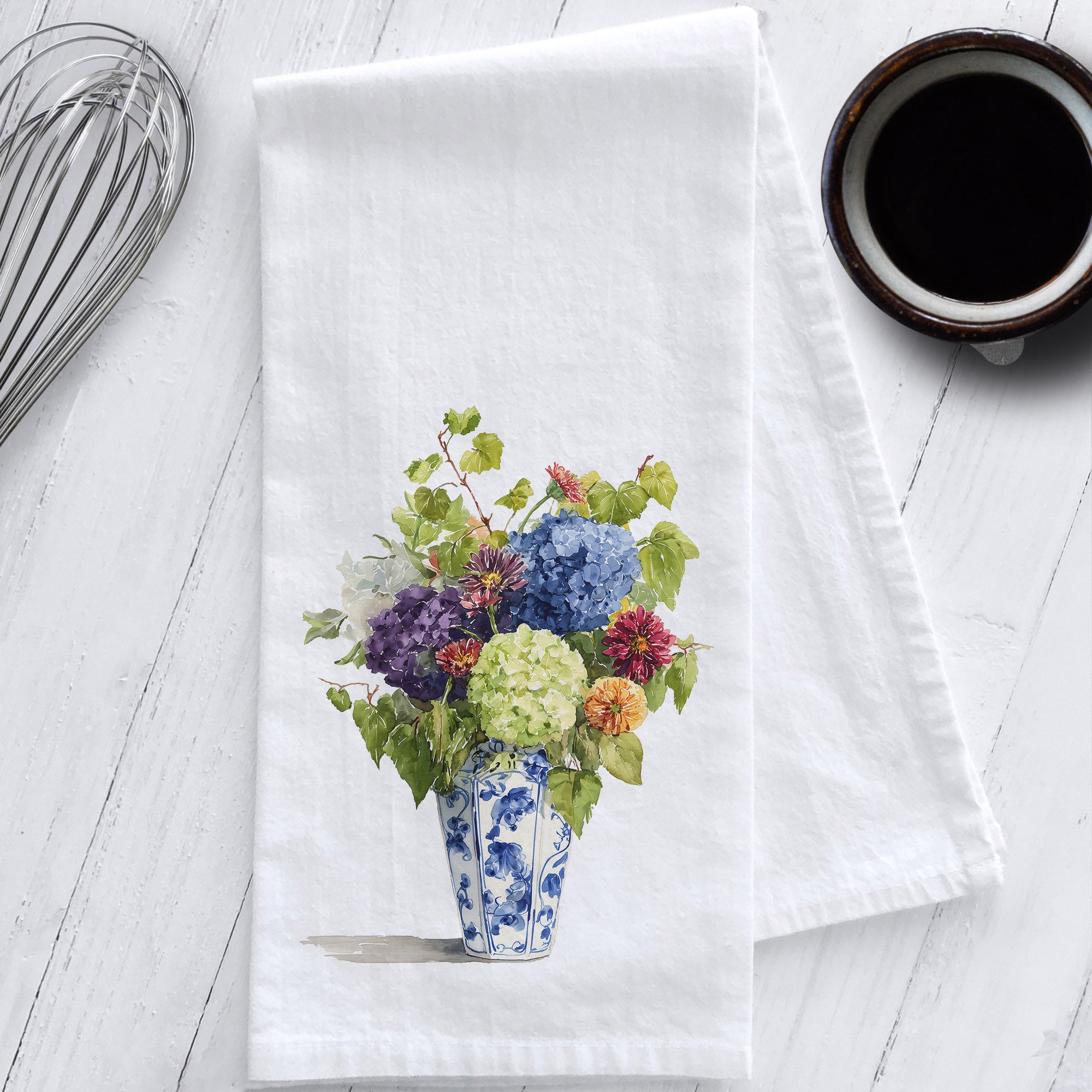 Floral design on a white towel with a cup of coffee and whisk in the background