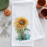 Load image into Gallery viewer, A white kitchen towel with a watercolor sunflower print, styled on a white marble surface with silverware, a small orange pumpkin, stacked plates, and two terracotta mugs.
